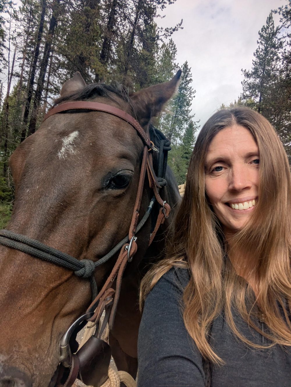 Monika smiling beside her bay mare on a forest trail