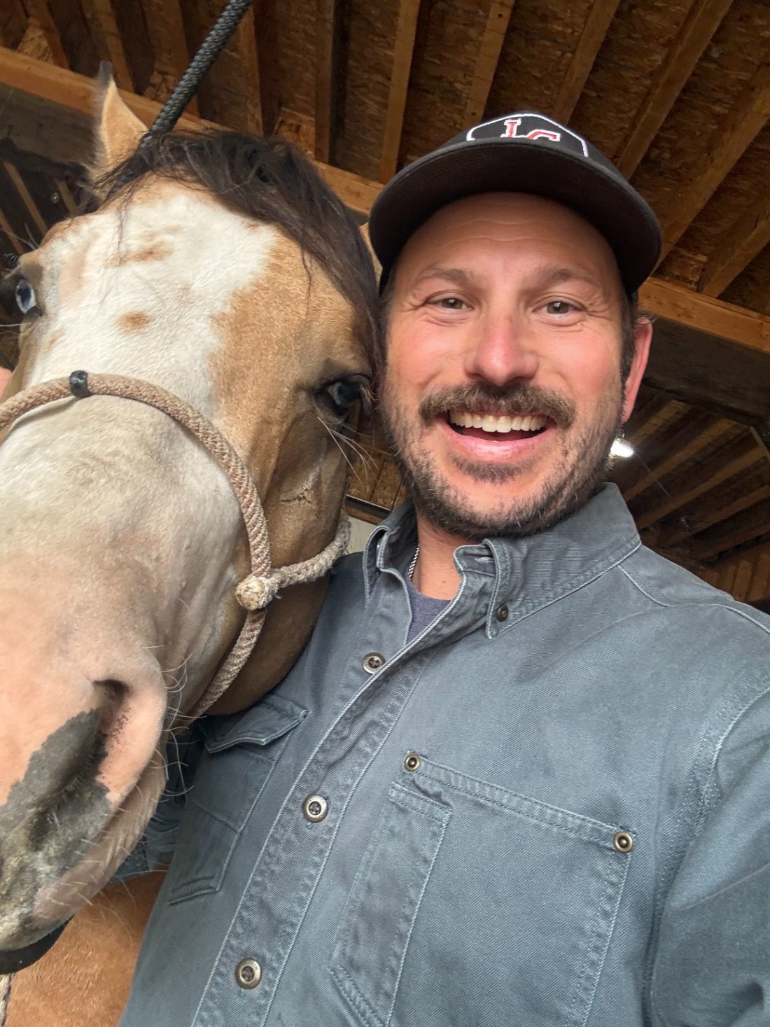 Dr. Austin smiling beside a buckskin horse in the barn